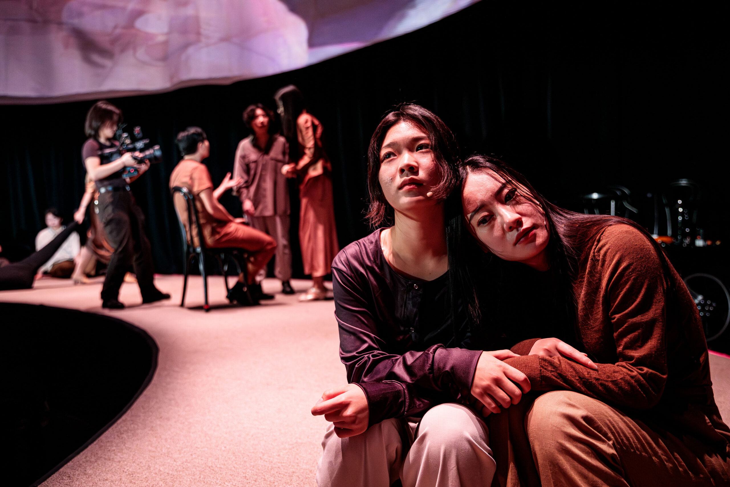 Photo of students performing A Dream Like a Dream. Two women in foreground finding comfort in each other.