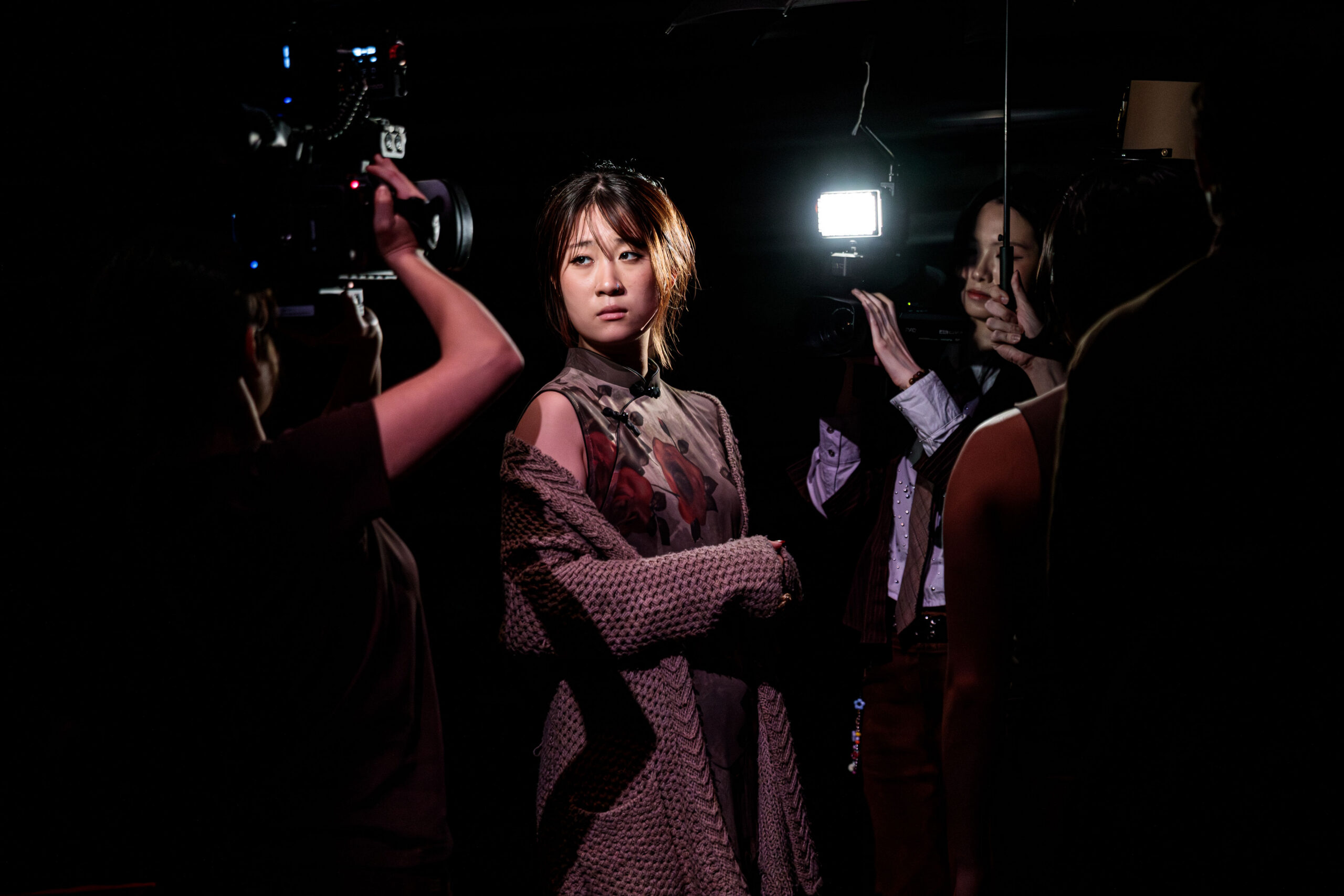 Production photo from a Dream Like a Dream. Woman being filmed in darkness. She is looking at one of the video cameras.
