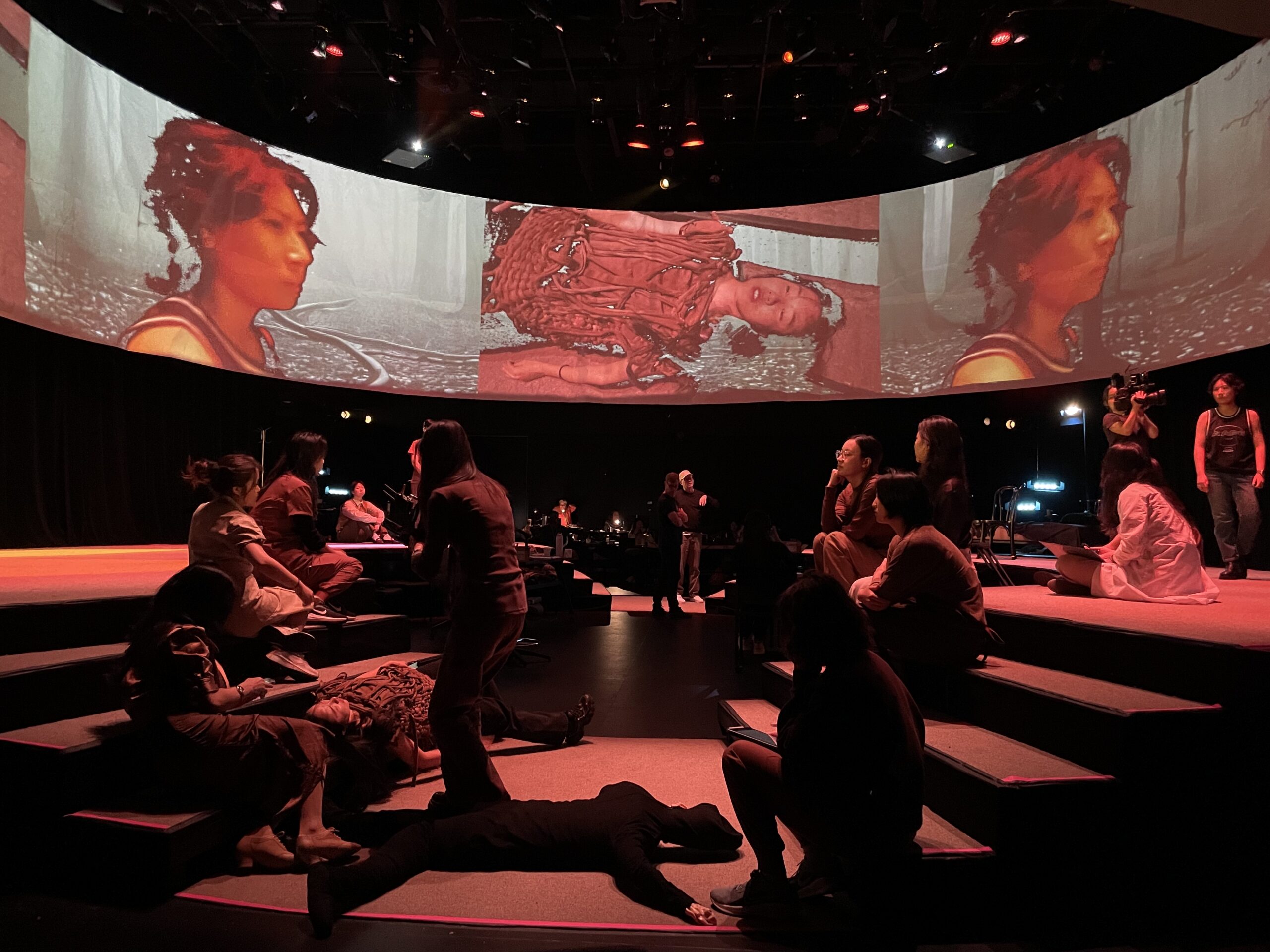Production photo from A Dream Like a Dream. Performers in front of a curved project screen with imagery above them.