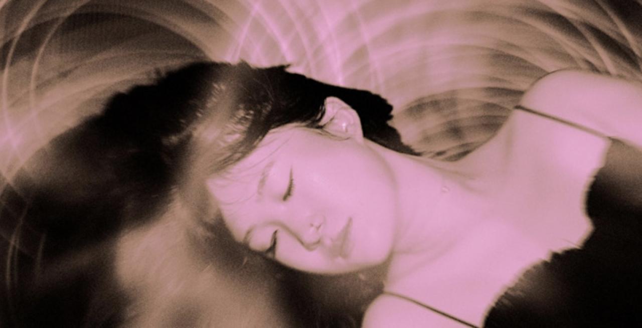 Pink and dark brown photo of a woman asleep and dreaming.
