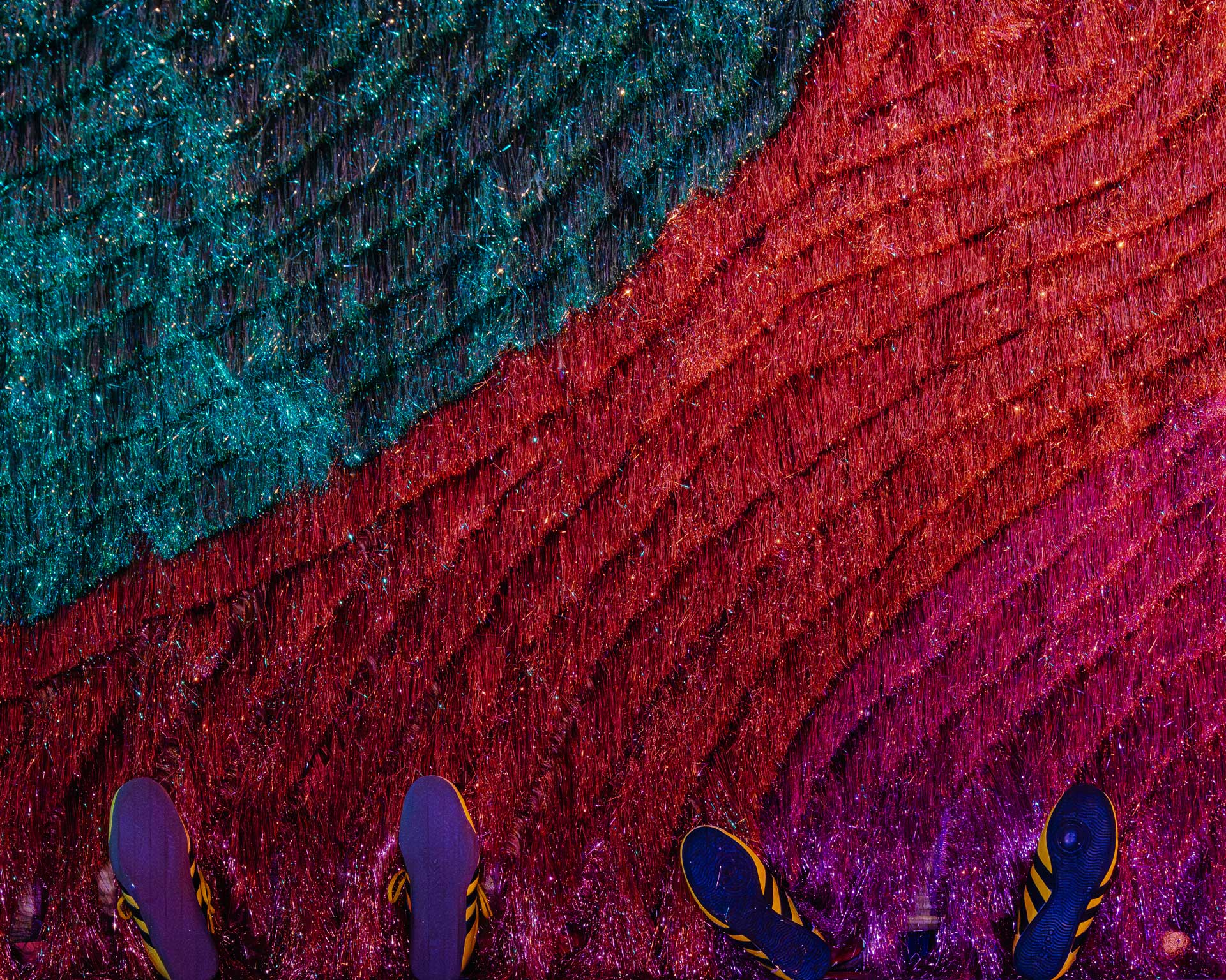 Two sets of shoes sticking out from beneath a colorful, textured wall.
