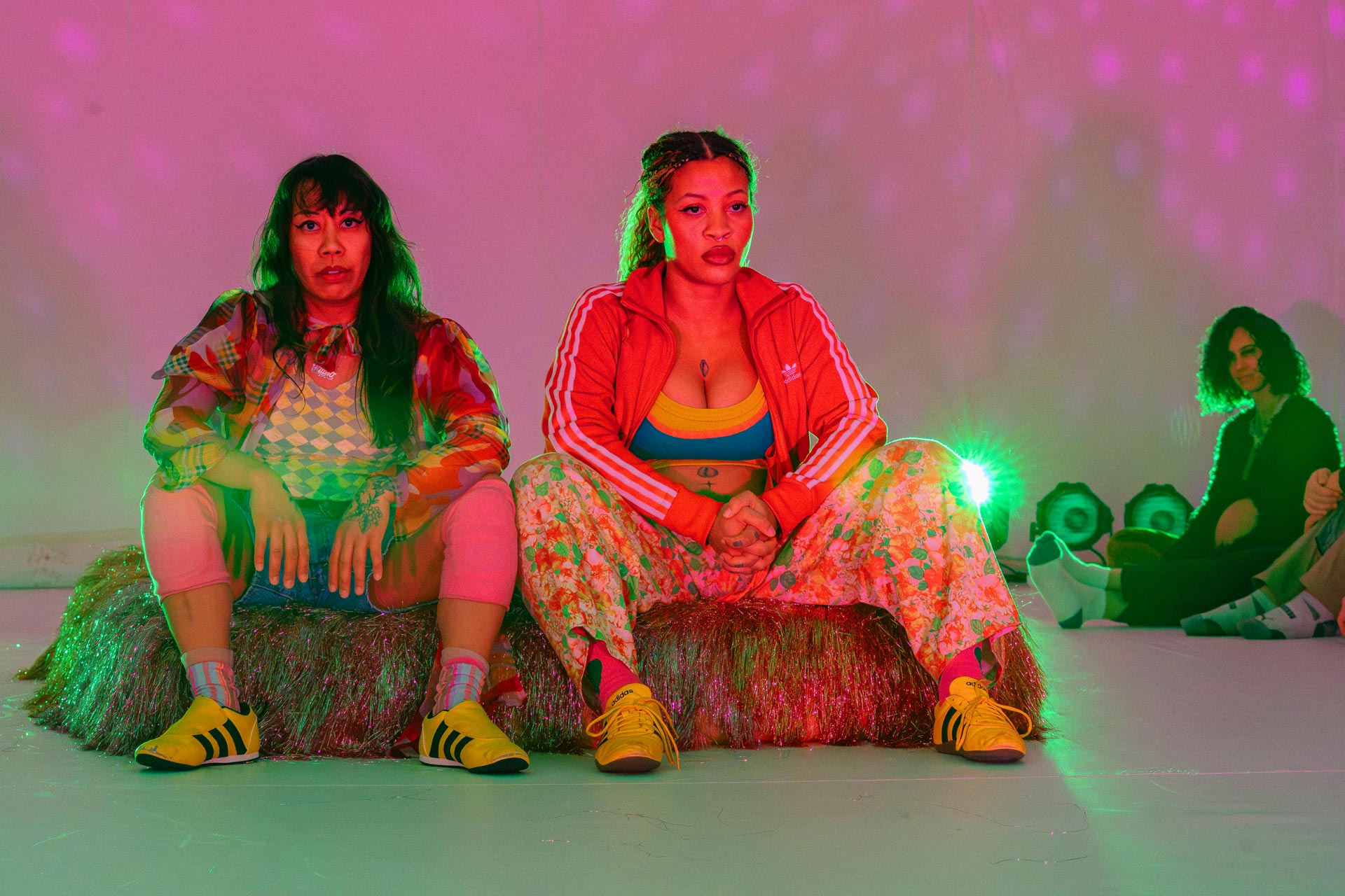 Dancers sitting on a theatrical bed in colorful clothing.