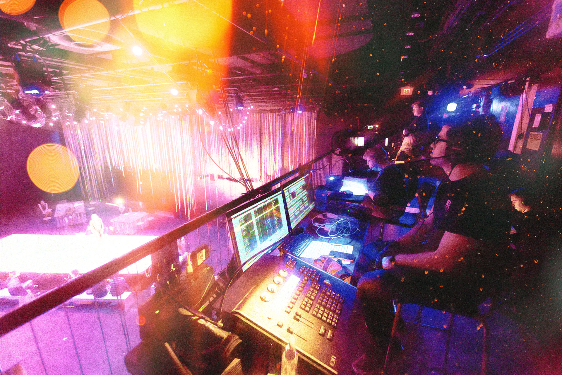 Student designers operating equipment from a sound and lighting booth.