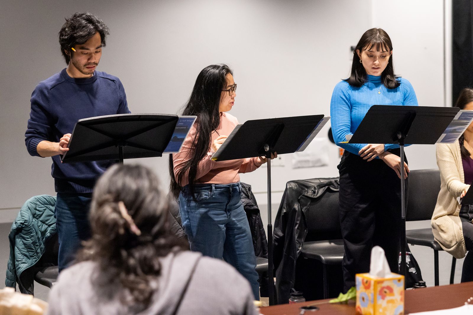 Multiple people during staged reading of a play script.